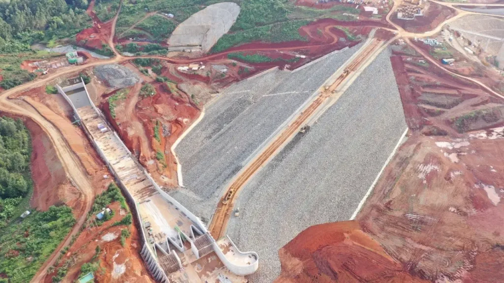 Spillway and dam embankment construction works at Karimenu II Dam showing rock fill placement and reinforced concrete spillway structures.