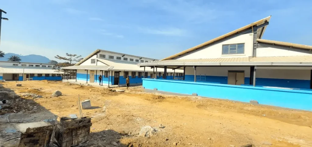 Steel portal frame hospital buildings under construction showing roof trusses, masonry walls, and site works.
